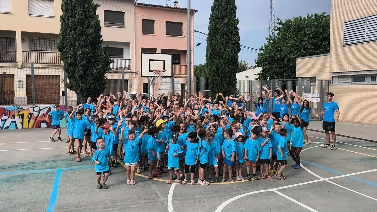 Tot el casal d'estiu, amb la samarreta blava, amb els braços enlaire a la pista de l'escola