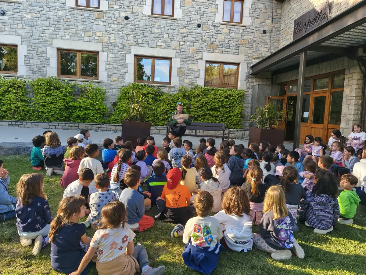 Infants asseguts a la gespa davant la casa de colònies de Vespella, escoltant un monitor