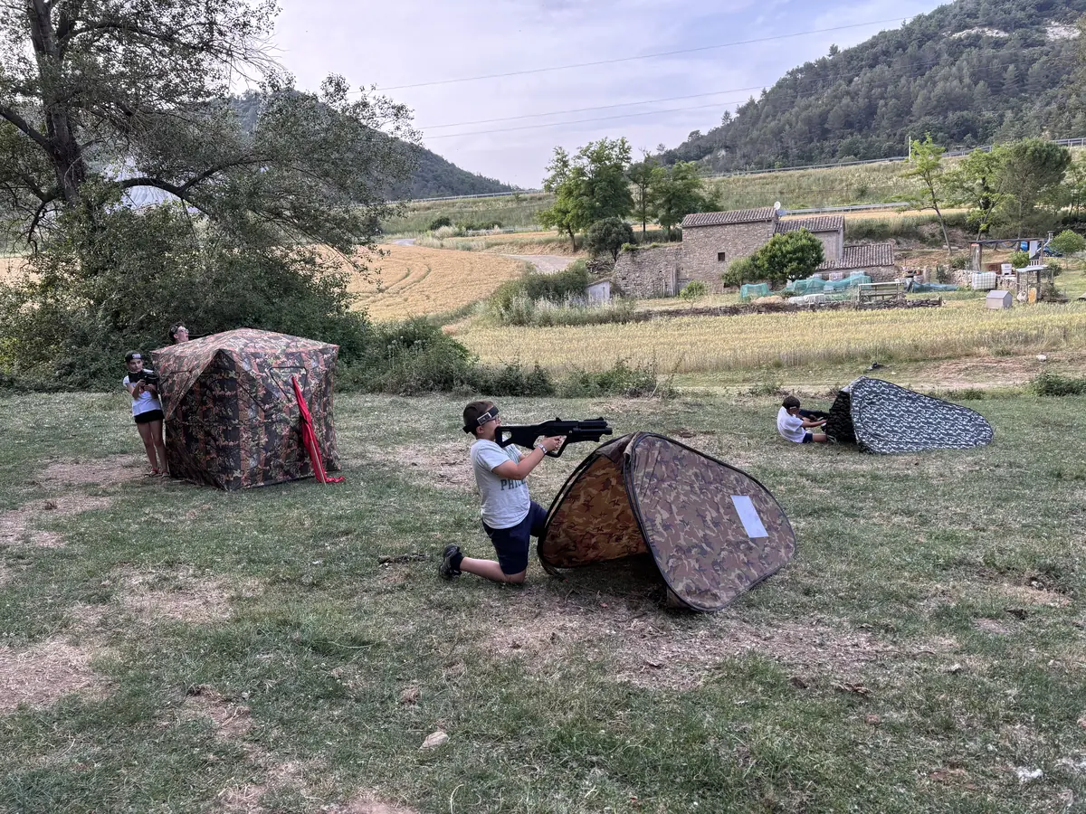 Camp de làser tag amb amagatalls de camuflatge en un prat, amb la muntanya al fons