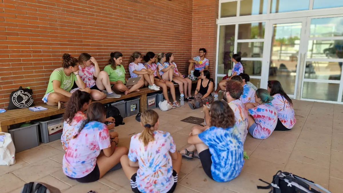Monitoratge i infants asseguts al porxo d'una escola, amb samarretes de colors
