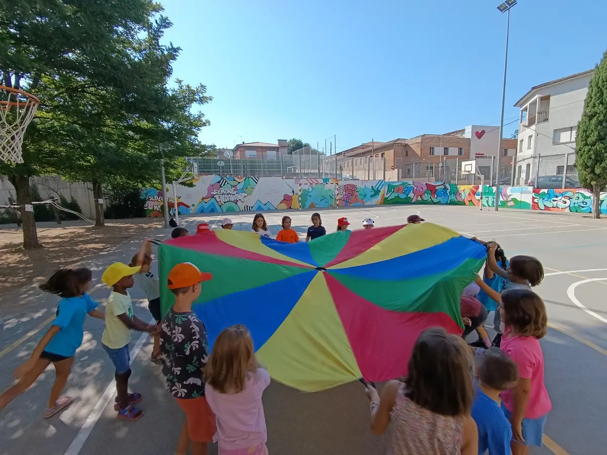 Infants fent voltar un paracaigudes de colors al pati d'una escola