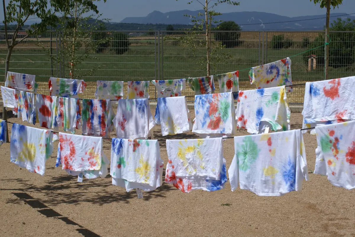 Samarretes tenyides de colors assecant-se en un estenedor, després d'un taller
