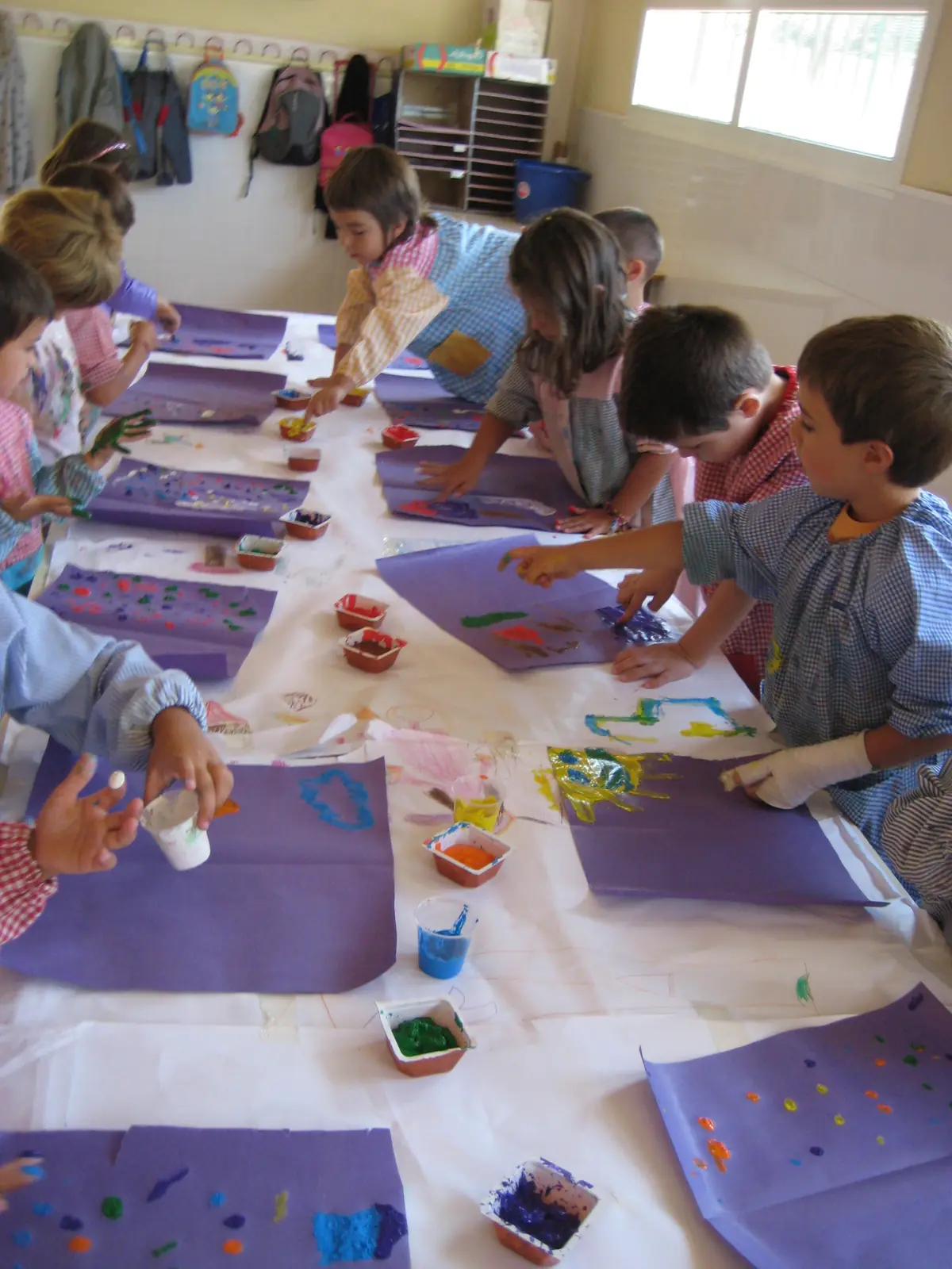 Infants pintant en una taula llarga coberta de paper, vistos des de dalt